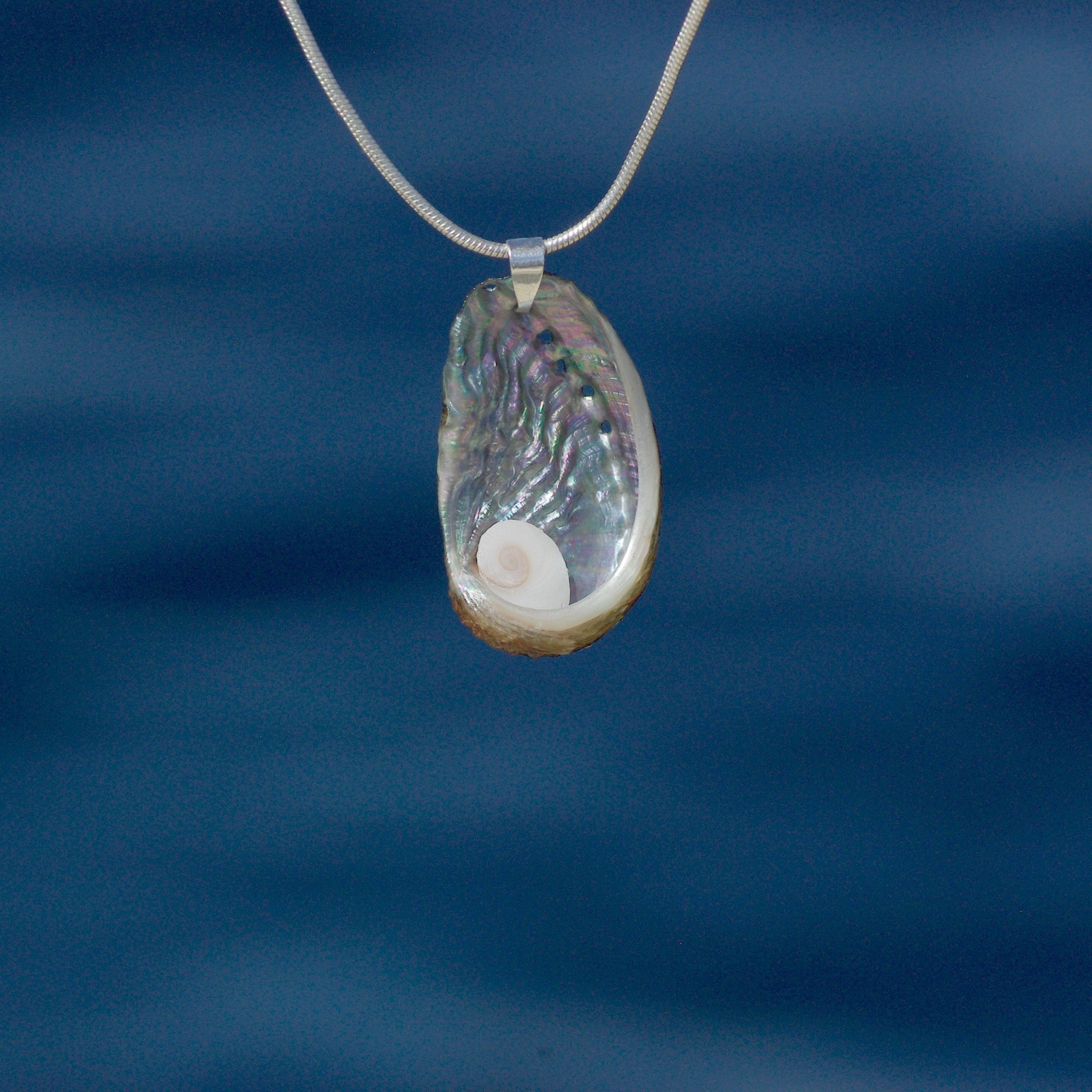 gros plan d'un pendentif coquillage ormeau avec un oeil de sainte lucie . photographié devant la mer.