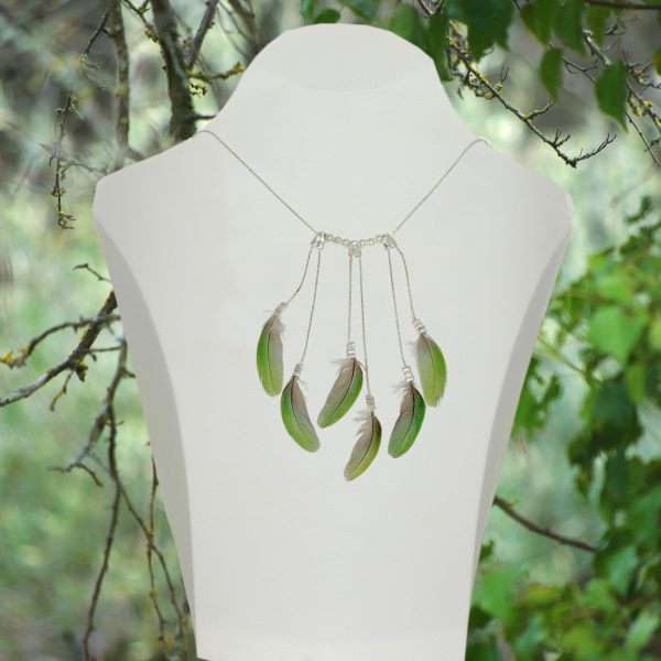 Un collier fait de chaînes argentées et de plumes vertes, présenté dans un décor végétal.