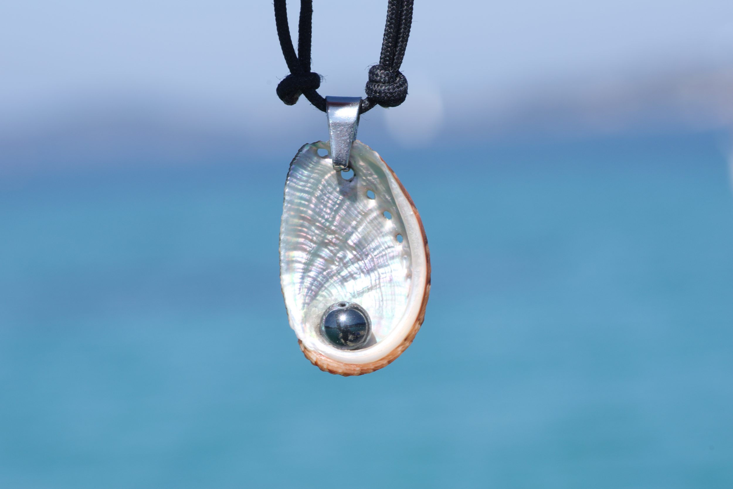 collier haliotis et hématite sur cordelette marine noire, sur fond de mer bleue