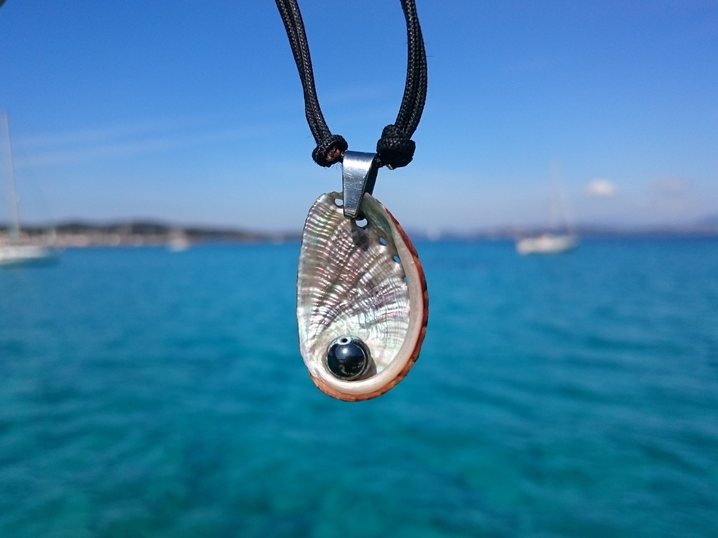collier haliotis et hématite sur bout marin noire, sur fond de mer bleue