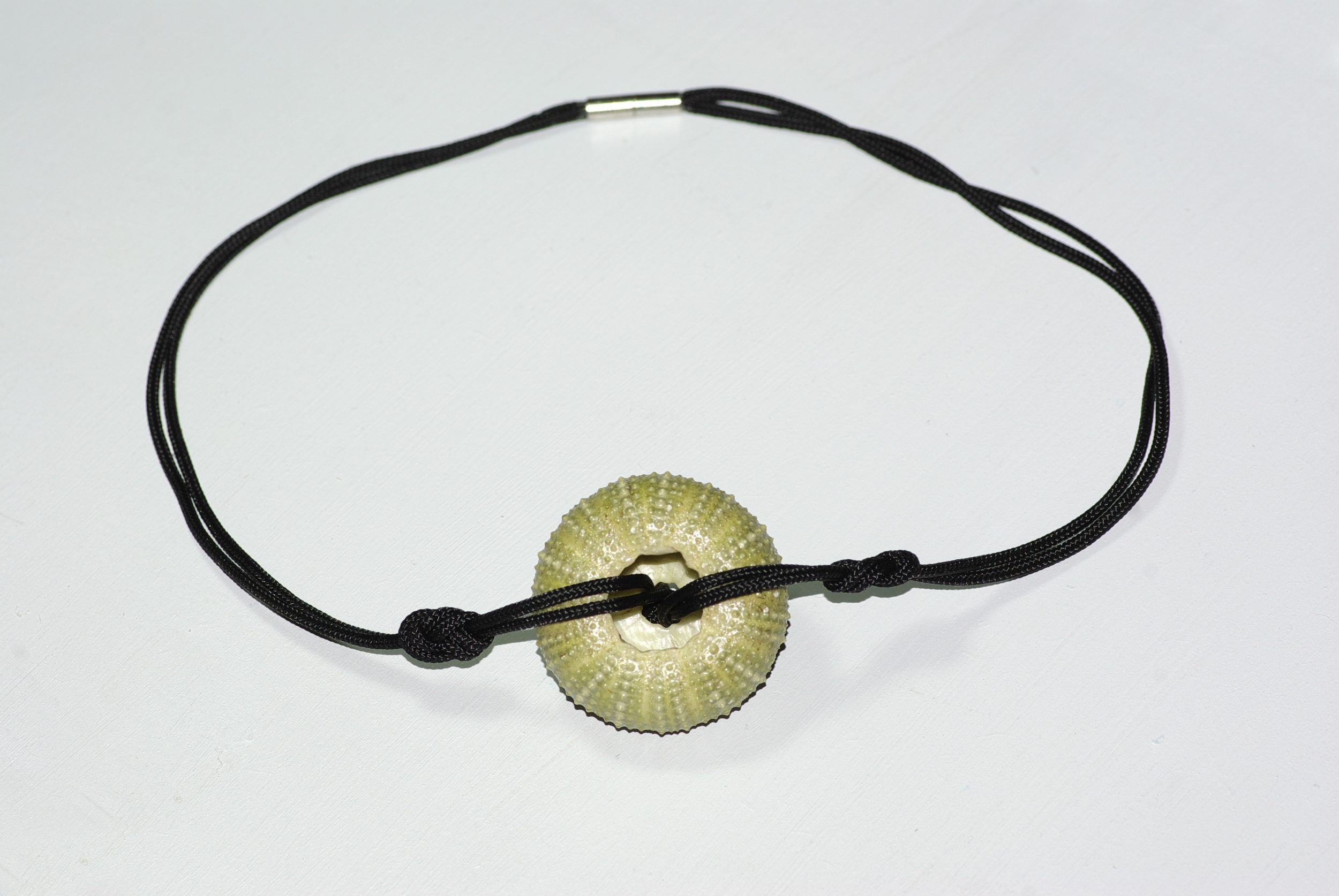 Collier avec un pendentif oursin vert sur une cordelette noire en polyester nouée façon marine. Vu de sos