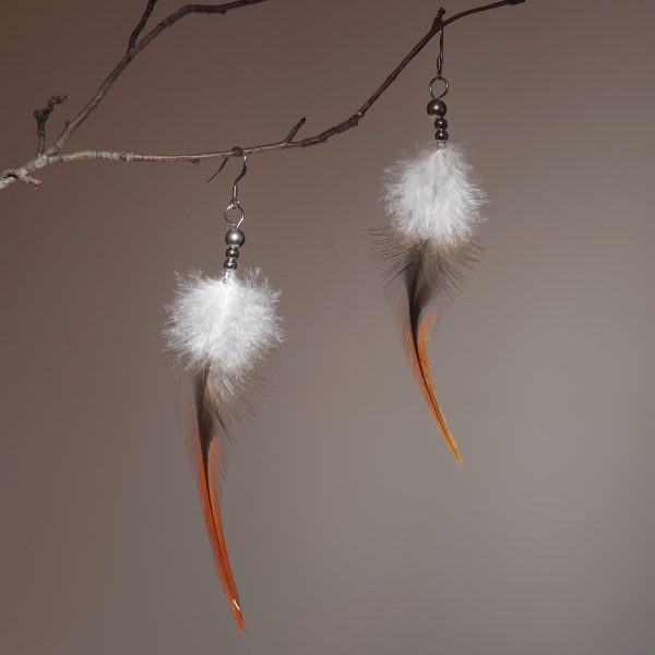 très longues plumes effilées marron avec une zone duveteuse blanche montées en boucles d'oreilles avec des perles en inox, photo en clair obscur