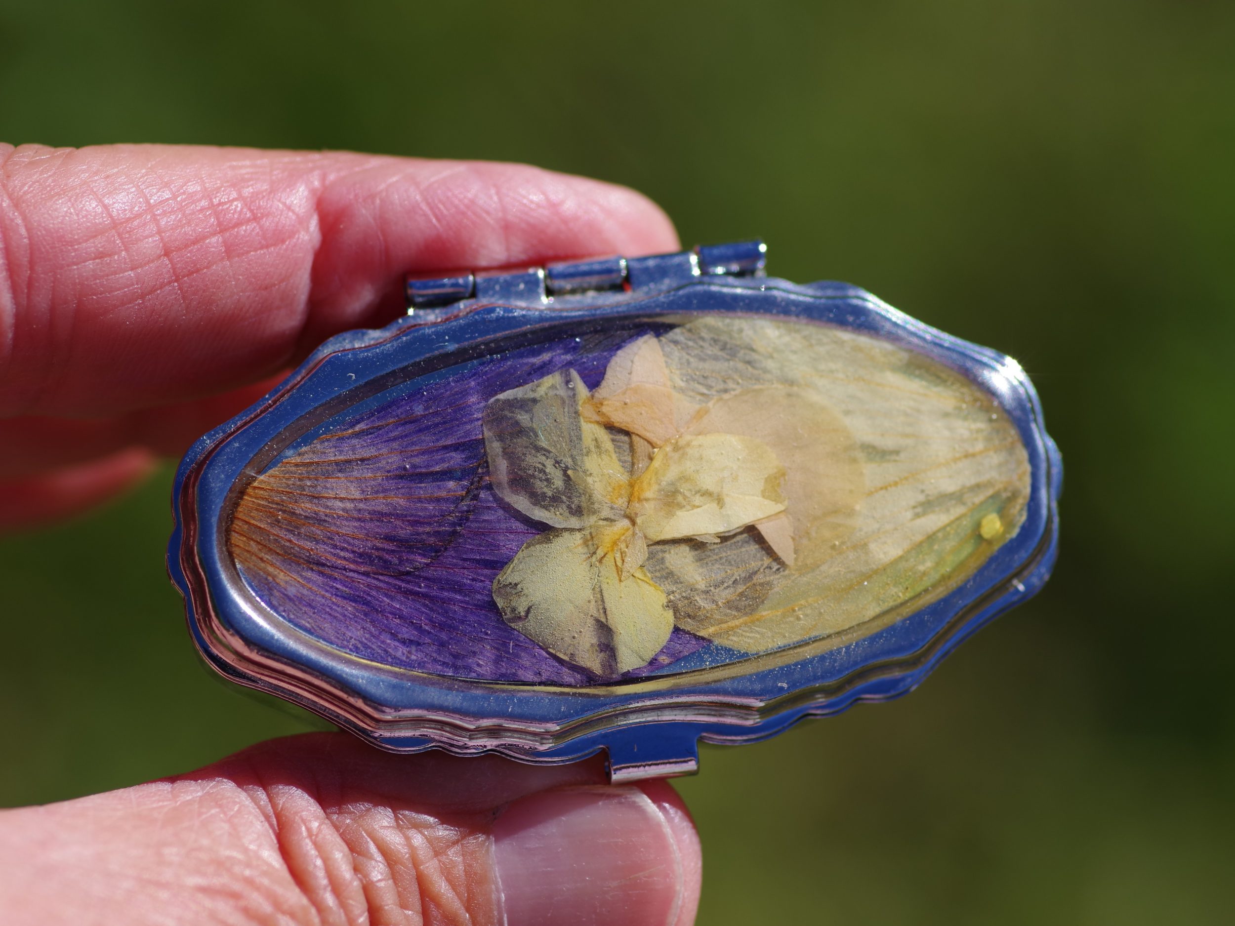 petite boite à pilule ovale joliment décorée de fleurs , décor bicolore violet et jaune, avec une mini pensée jaune. Le boitier est argenté