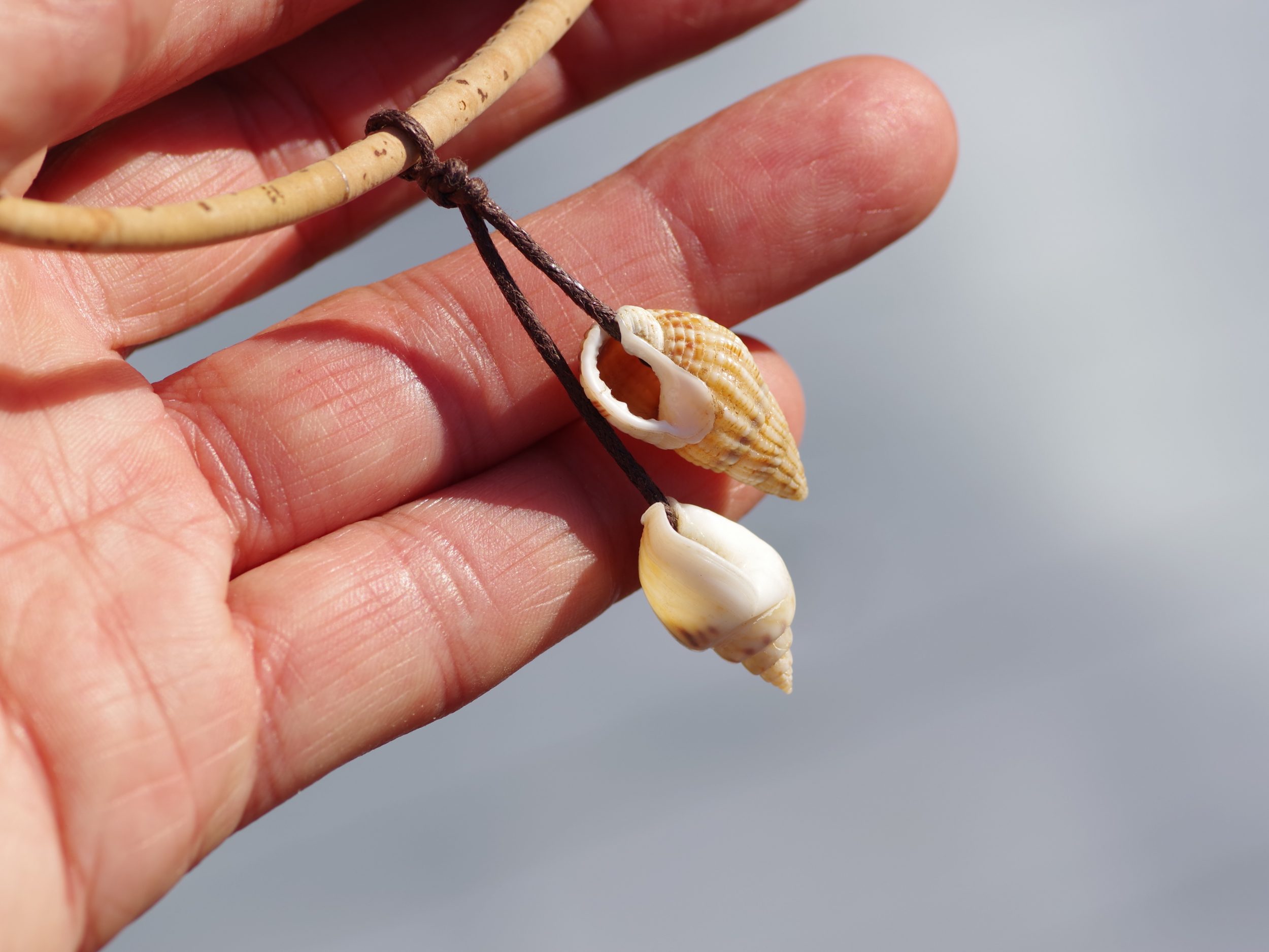original pendentif coquillages : deux coquillages beiges et bmancs de type escargot marins pointus reliés par un fin cordon de coton, collier en liège beige naturel