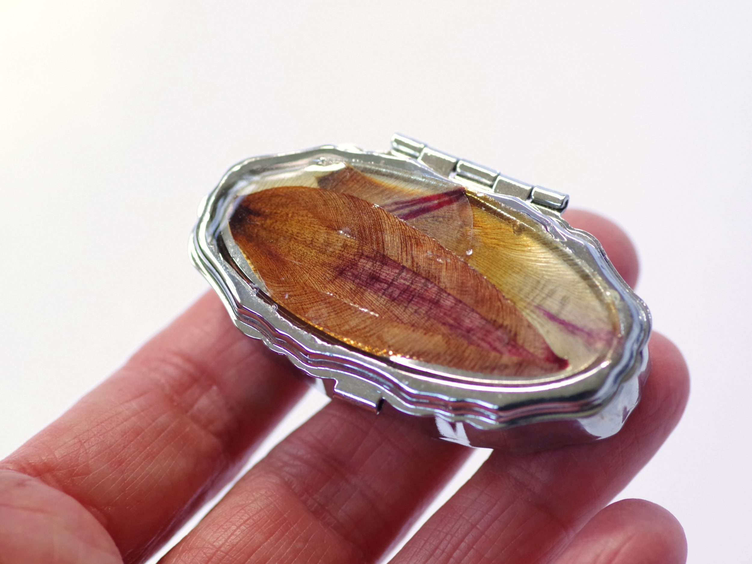 petite boite à pilules ovale décorée de pétales dans des tons orangés, boitier métallique argenté