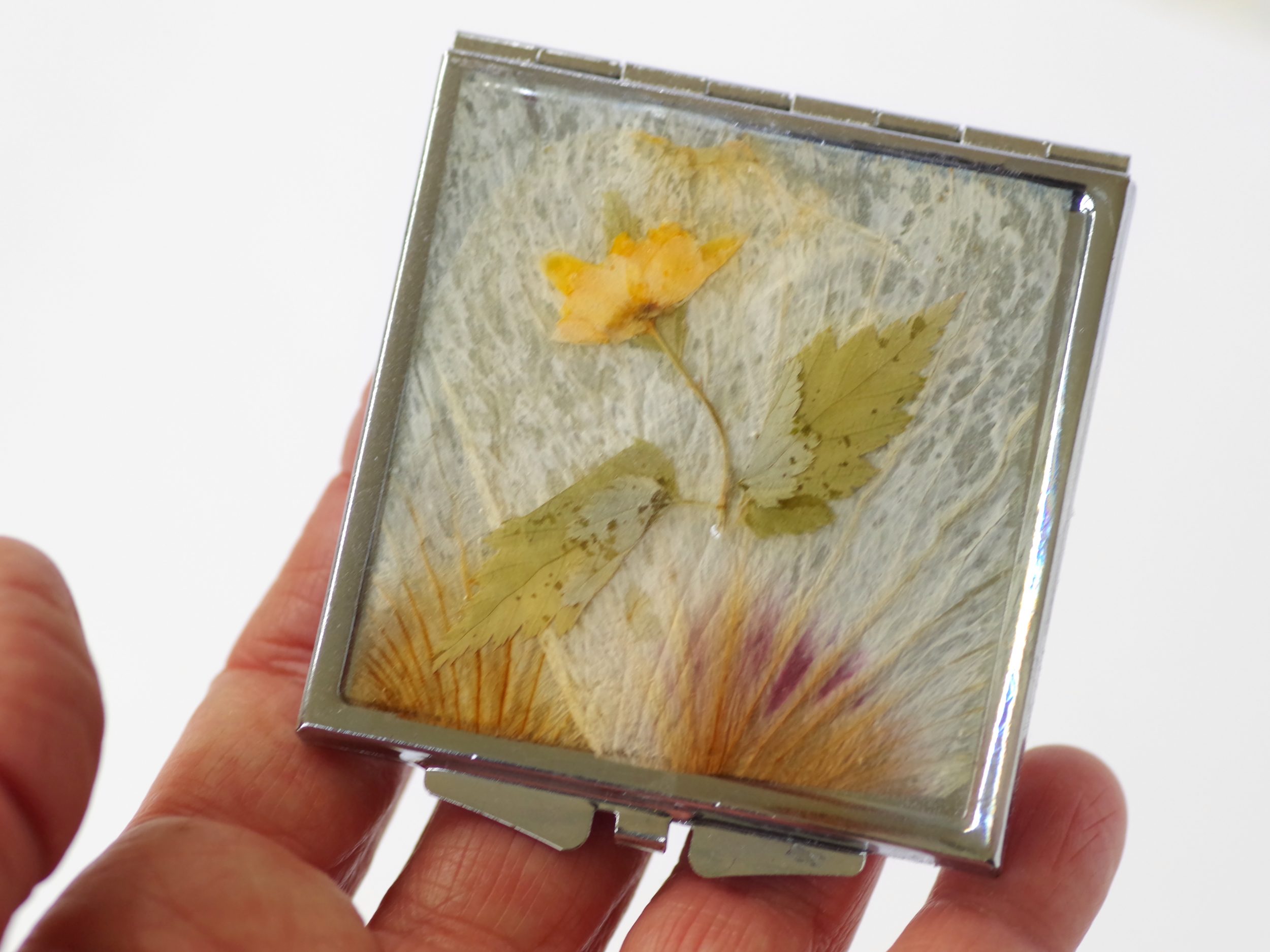 miroir de poche à décor floral : une petite fleur jaune sur un fond de pétales pâles, boîtier argenté