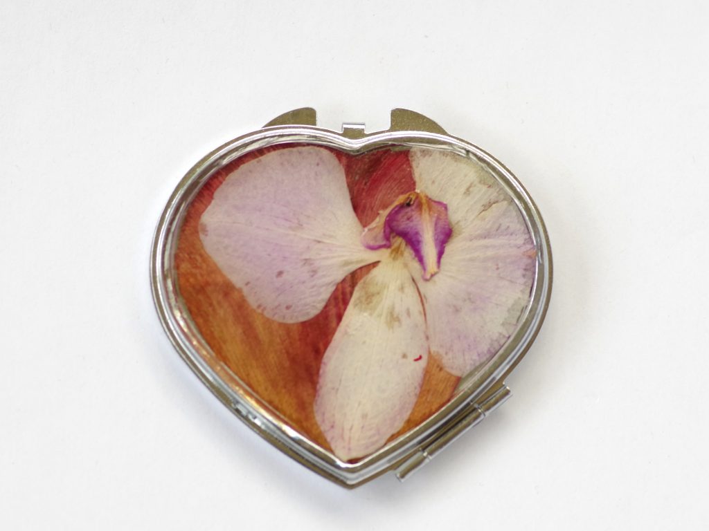 miroir de poche en forme de coeur décoré d'une orchidée parme sur fond rouge orangé, boitier métal argenté
