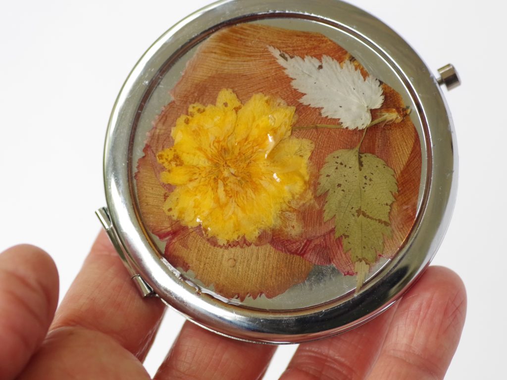 miroir de poche rond avec un décor champêtre : fleur jaune sur fond de pétales couleur rouille