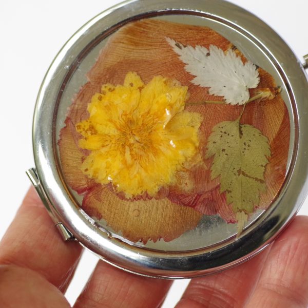 miroir de poche rond avec un décor champêtre : fleur jaune sur fond de pétales couleur rouille