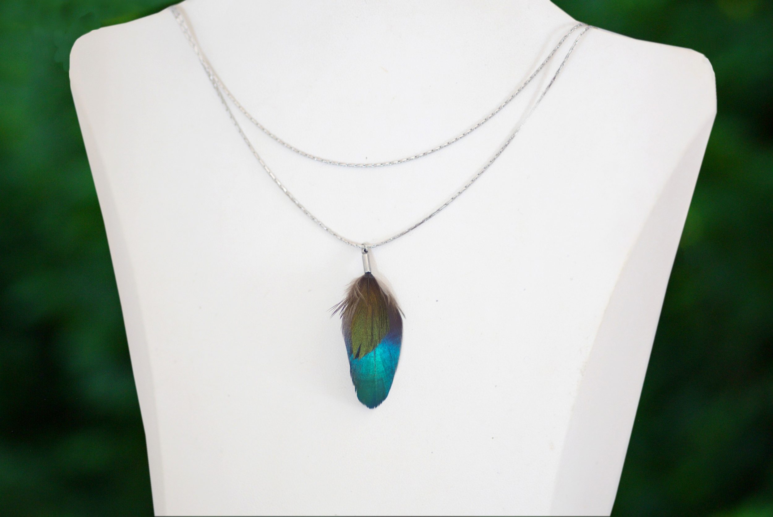 collier composé de deux fines chaînes argentées et un pendentif avec deux plumes brillantes : une bleue et une petite verte