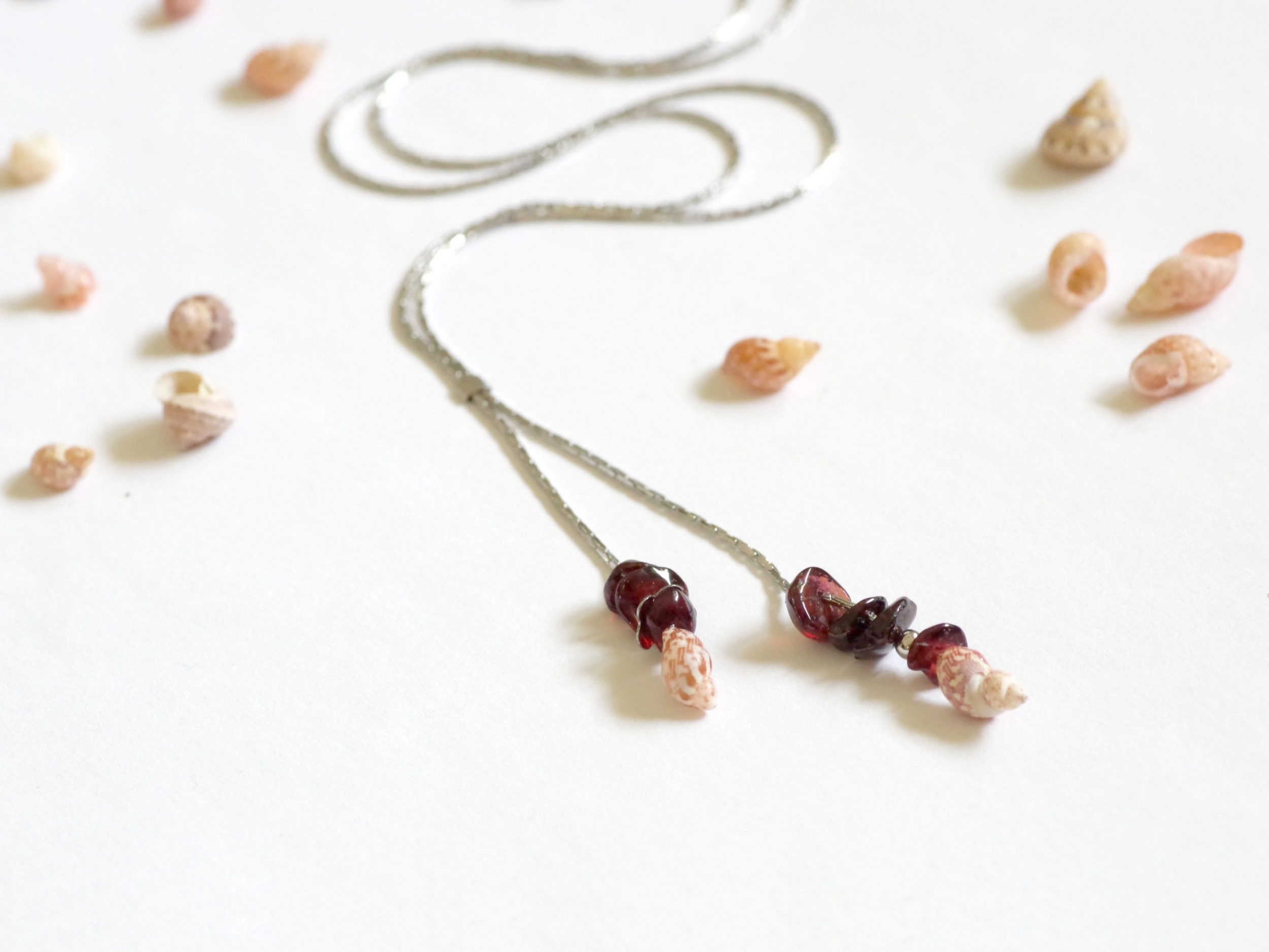 collier minimaliste : chaîne très fine en inox , les deux bouts de la chaîne forment deux pendentifs, avec quelques pierres de grenats et un mini coquillage