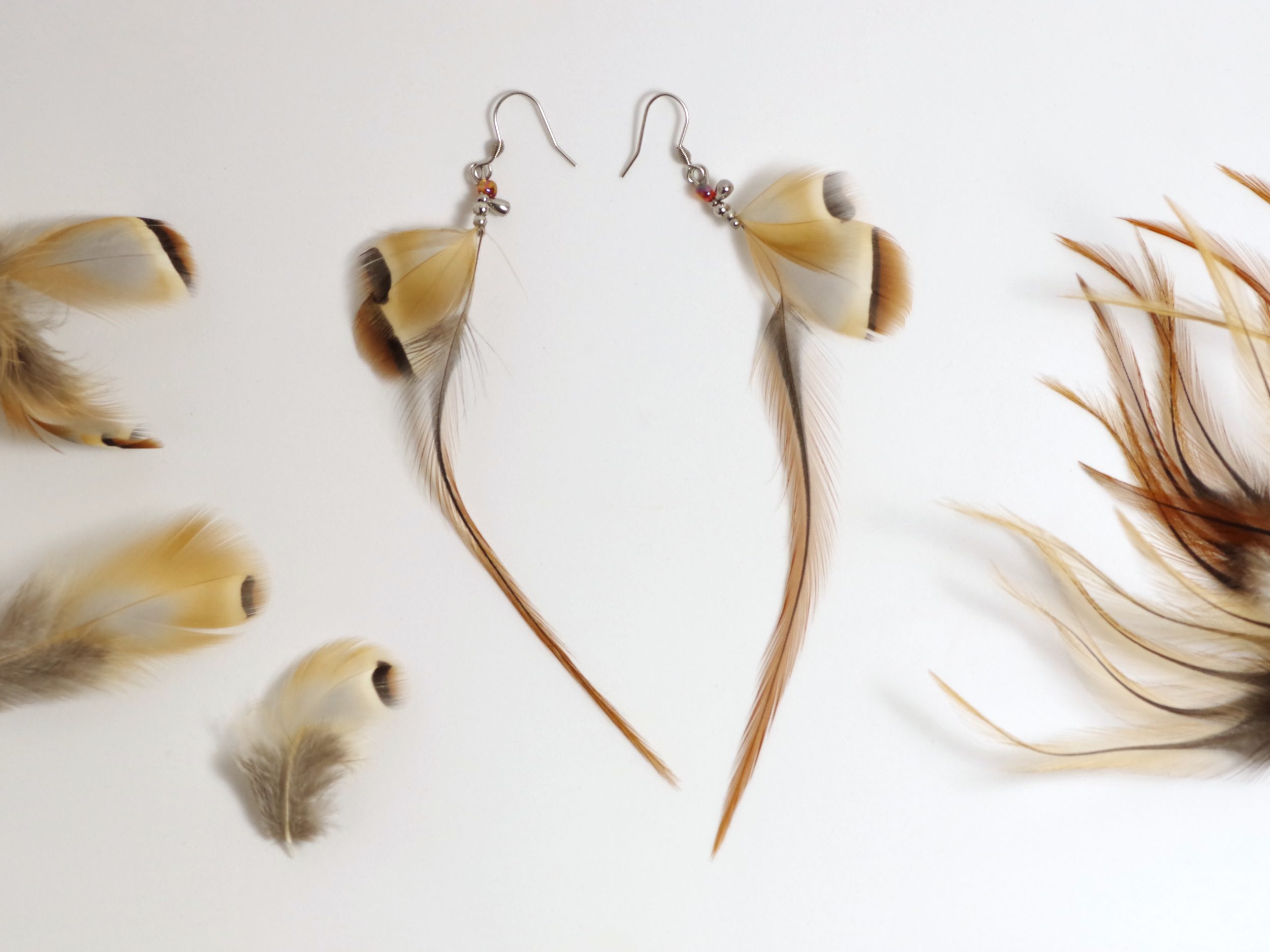 boucles d'oreilles aux longues et fines plumes marron associées à des petites plumes grises et marron.