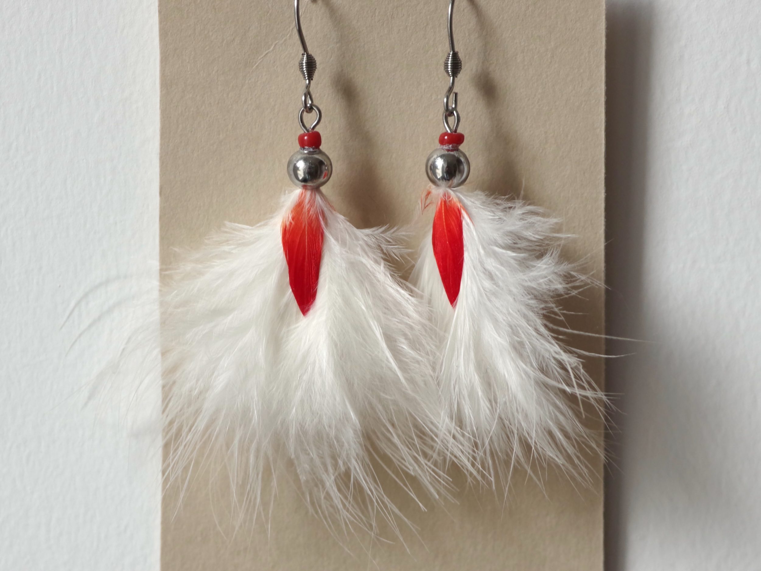 boucles d'oreilles rouge et blanc, plumes duveteuses blanches disposées en pompon, avec une petite plume rouge au milieu