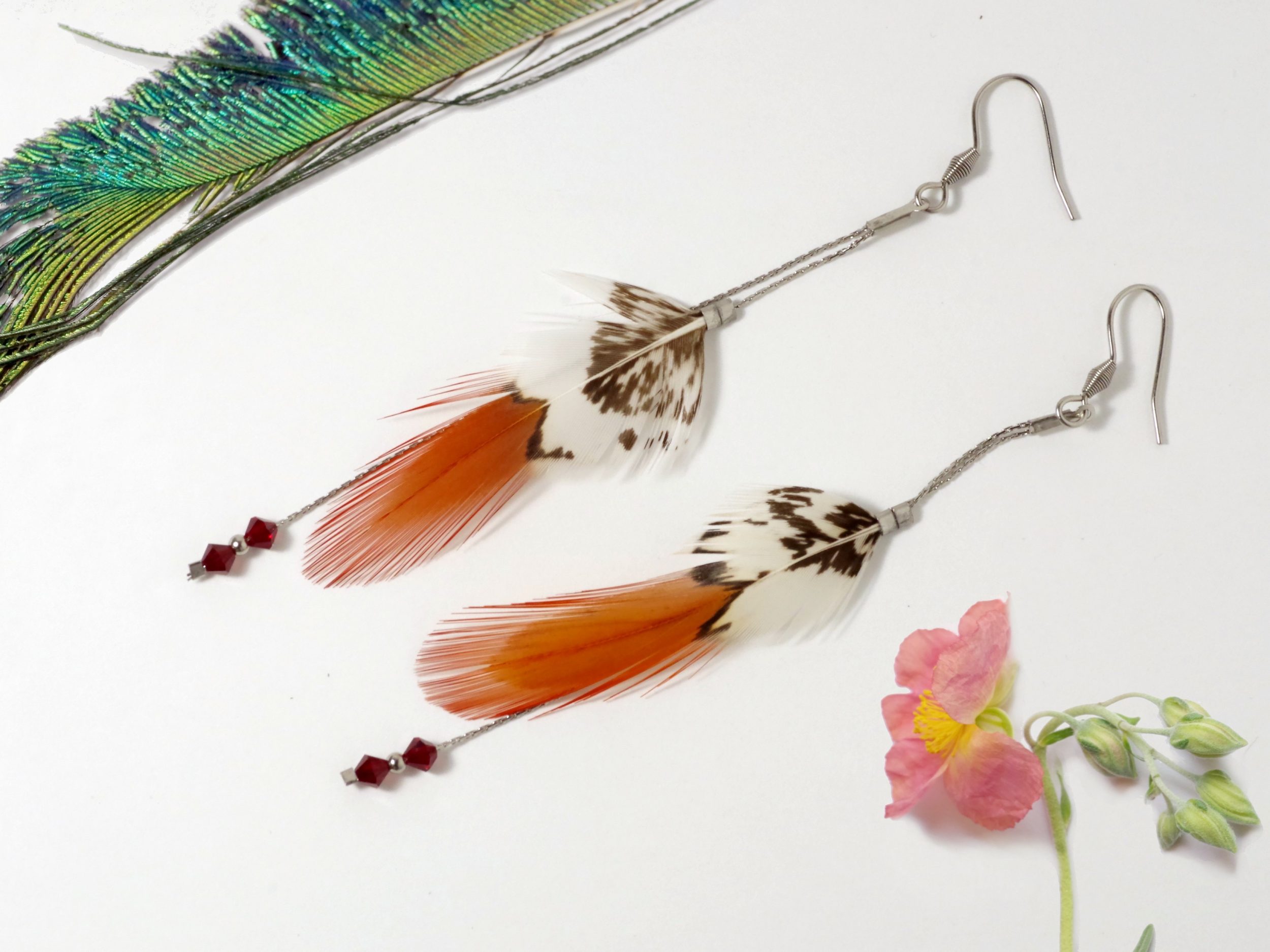 Boucles d'oreilles à plume rouge et blanche sur des chaînes en inox, accompagnées de perles rouges.