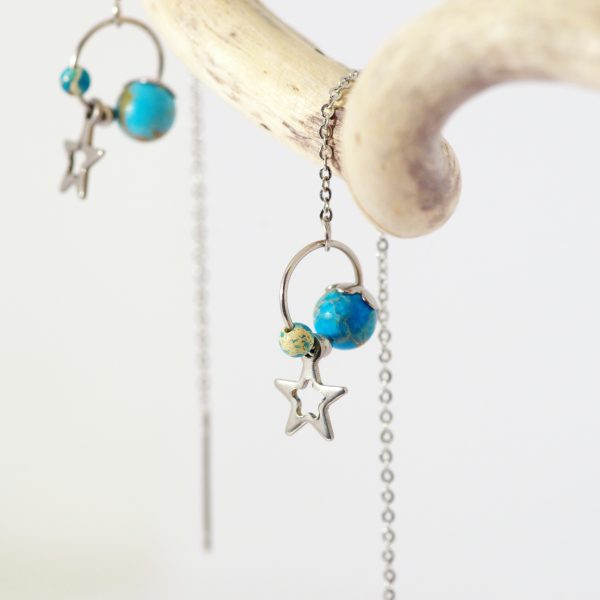Chaines d'oreilles avec deux perles bleues ressemblant à des planètes et une étoile argentée montées sur un anneau.