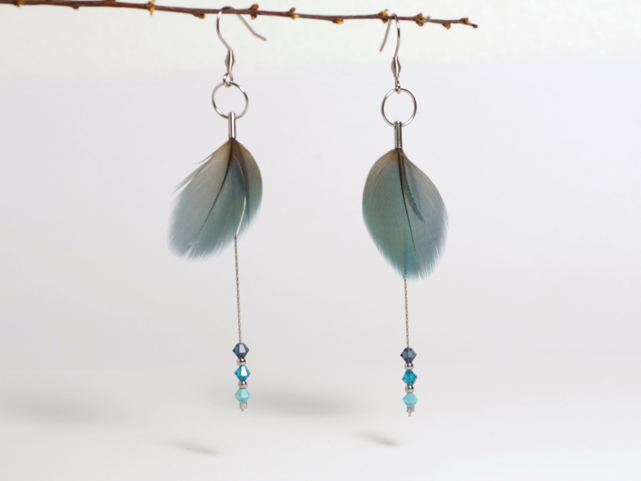 Boucles d'oreilles en plumes bleues et chaînes inox avec des petites perles facettées assorties.