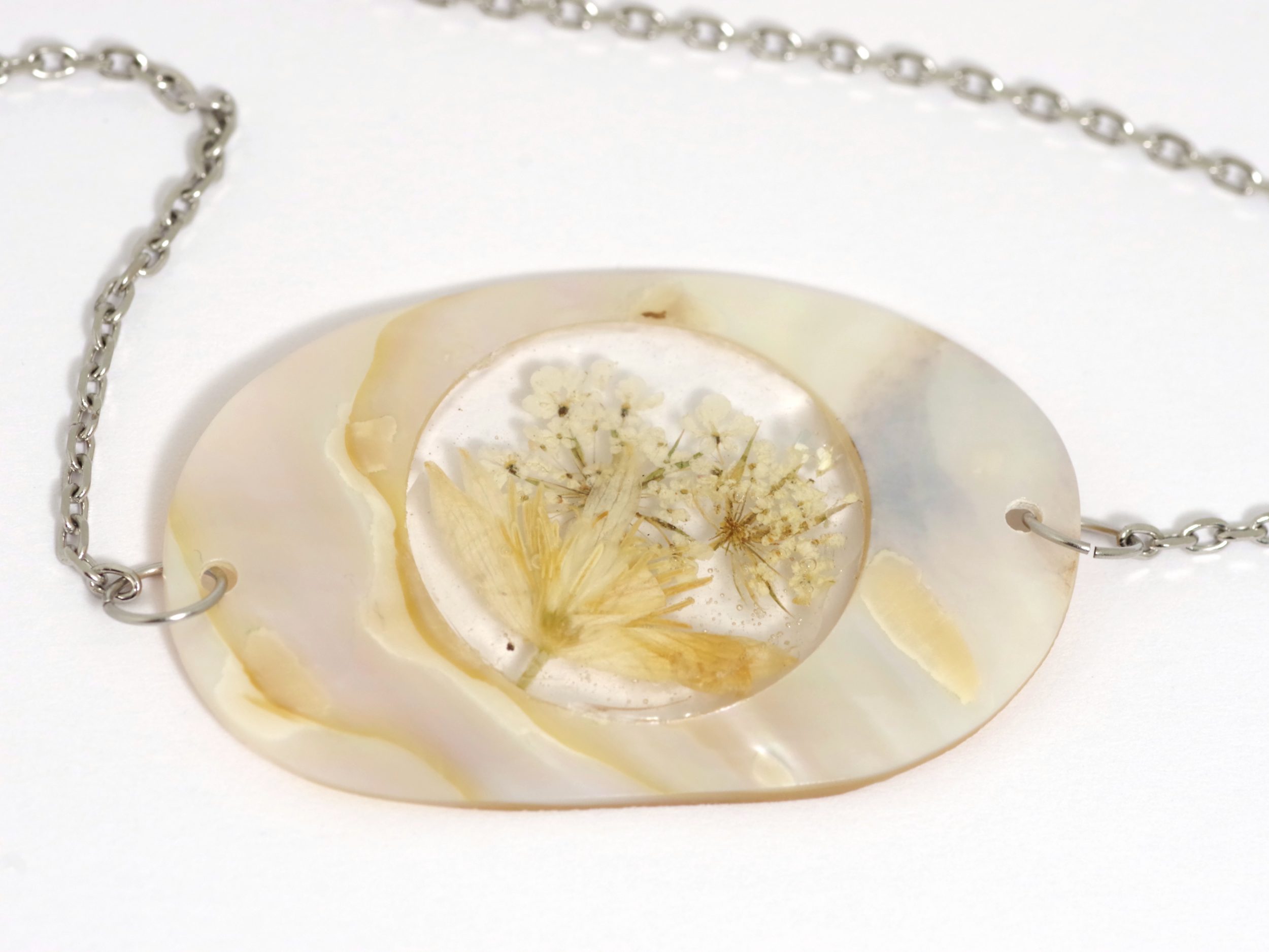 pendentif de nacre avec un bouquet de fleurs blanches en inclusion dans de la résine transparente, chaîne inox