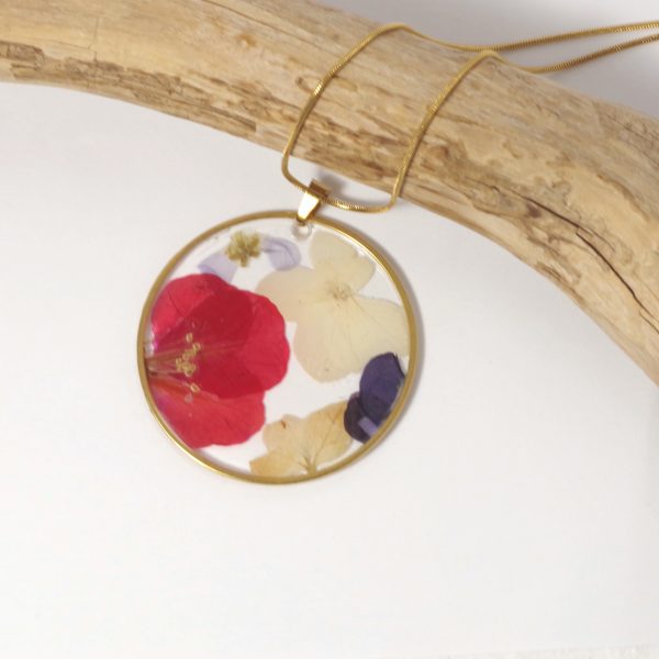 Une fleur rouge vif et des petites fleurs blanches en inclusion dans un pendentif doré.