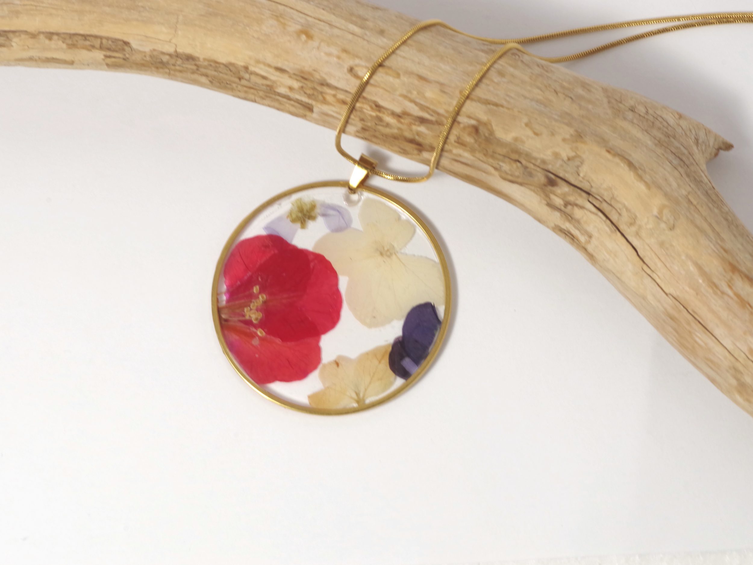 Une fleur rouge vif et des petites fleurs blanches en inclusion dans un pendentif doré.