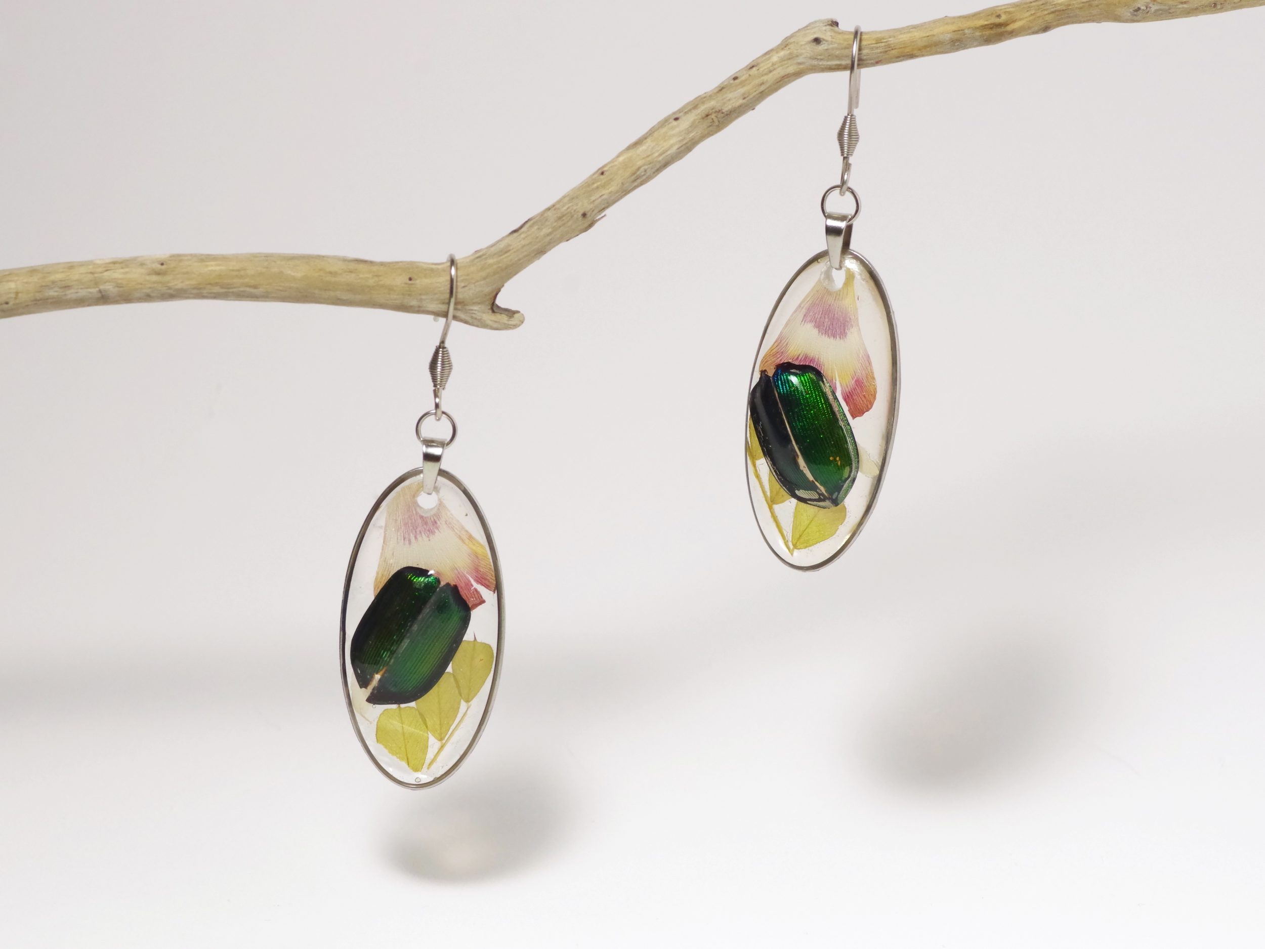 Boucles d'oreilles pendantes avec des petits élytres de scarabées, des fougères et des pétales en inclusion dans de la résine.