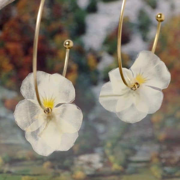 Des boucles d'oreilles nature avec des petites pensées blanches et jaunes sur de grandes créoles en inox doré.