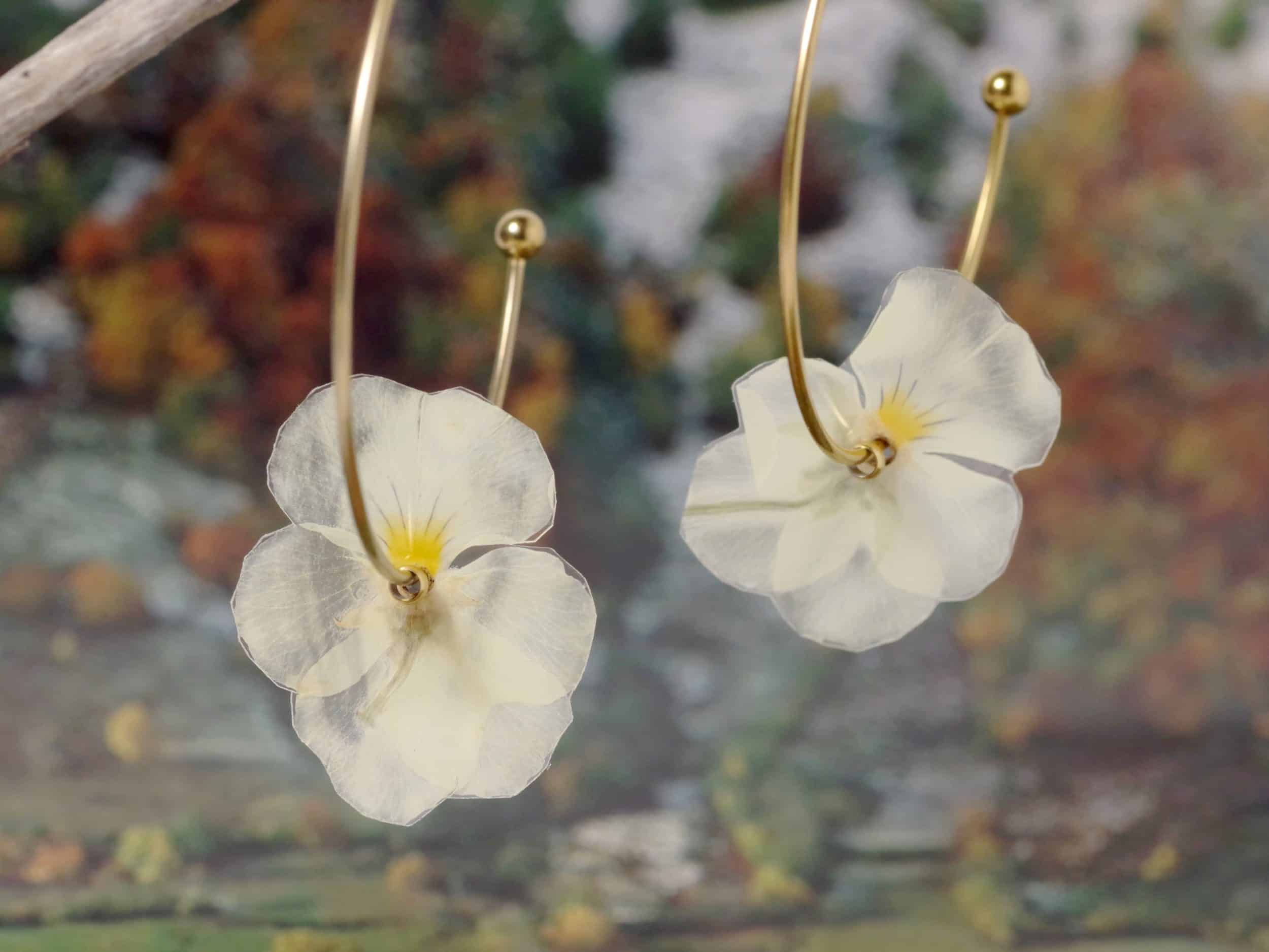 Des boucles d'oreilles nature avec des petites pensées blanches et jaunes sur de grandes créoles en inox doré.