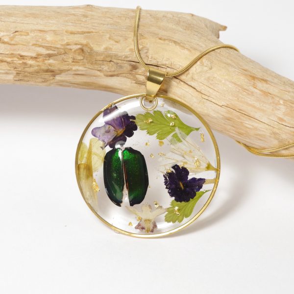 Un pendentif avec une composition naturaliste : petit scarabée et fleurs du jardin. Sur une chaine dorée.