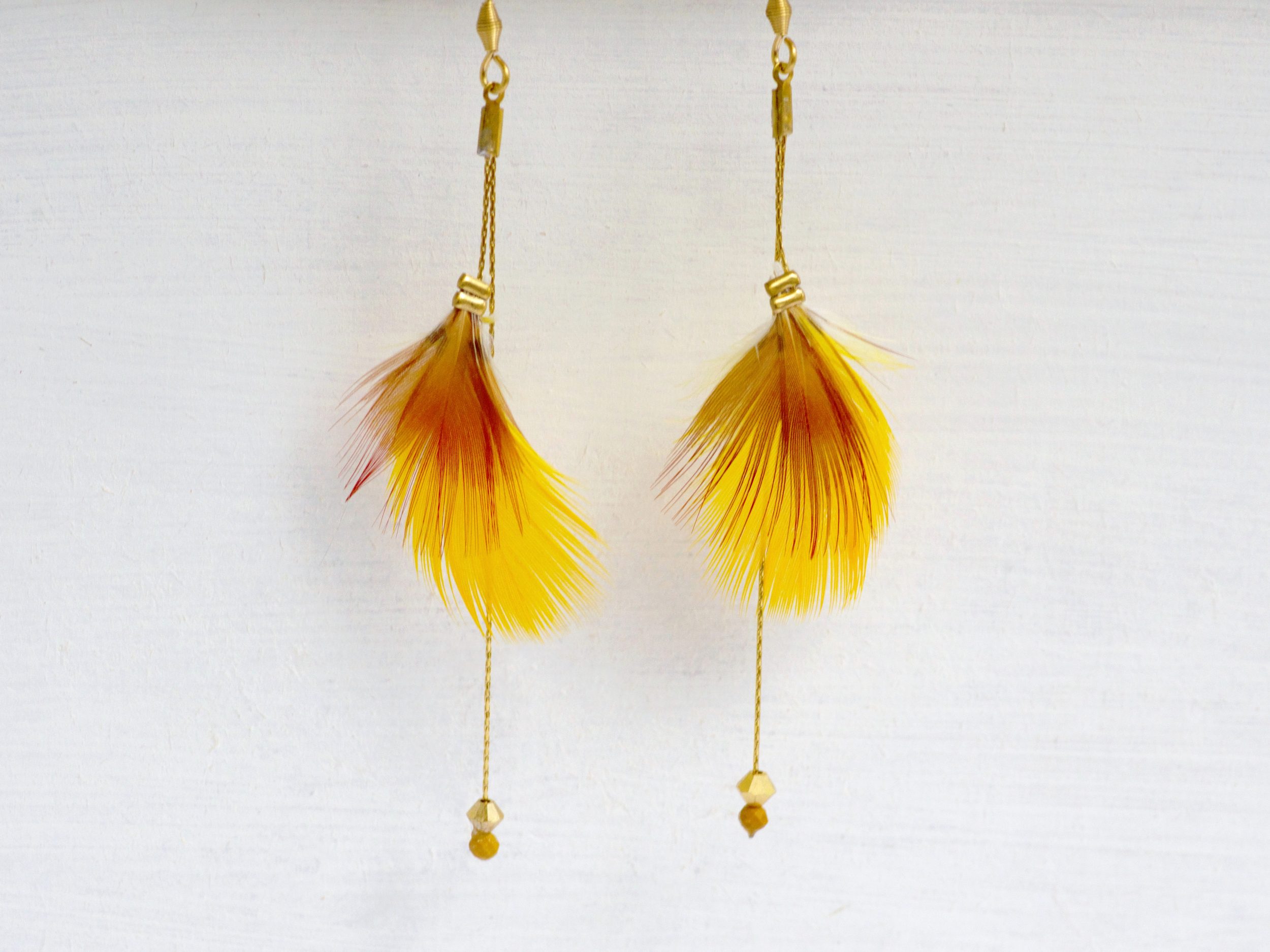 Plumes jaunes et rouges associées à des fines chaînes dorées et des perles de cristal, pour des boucles d'oreilles originales et féminines.
