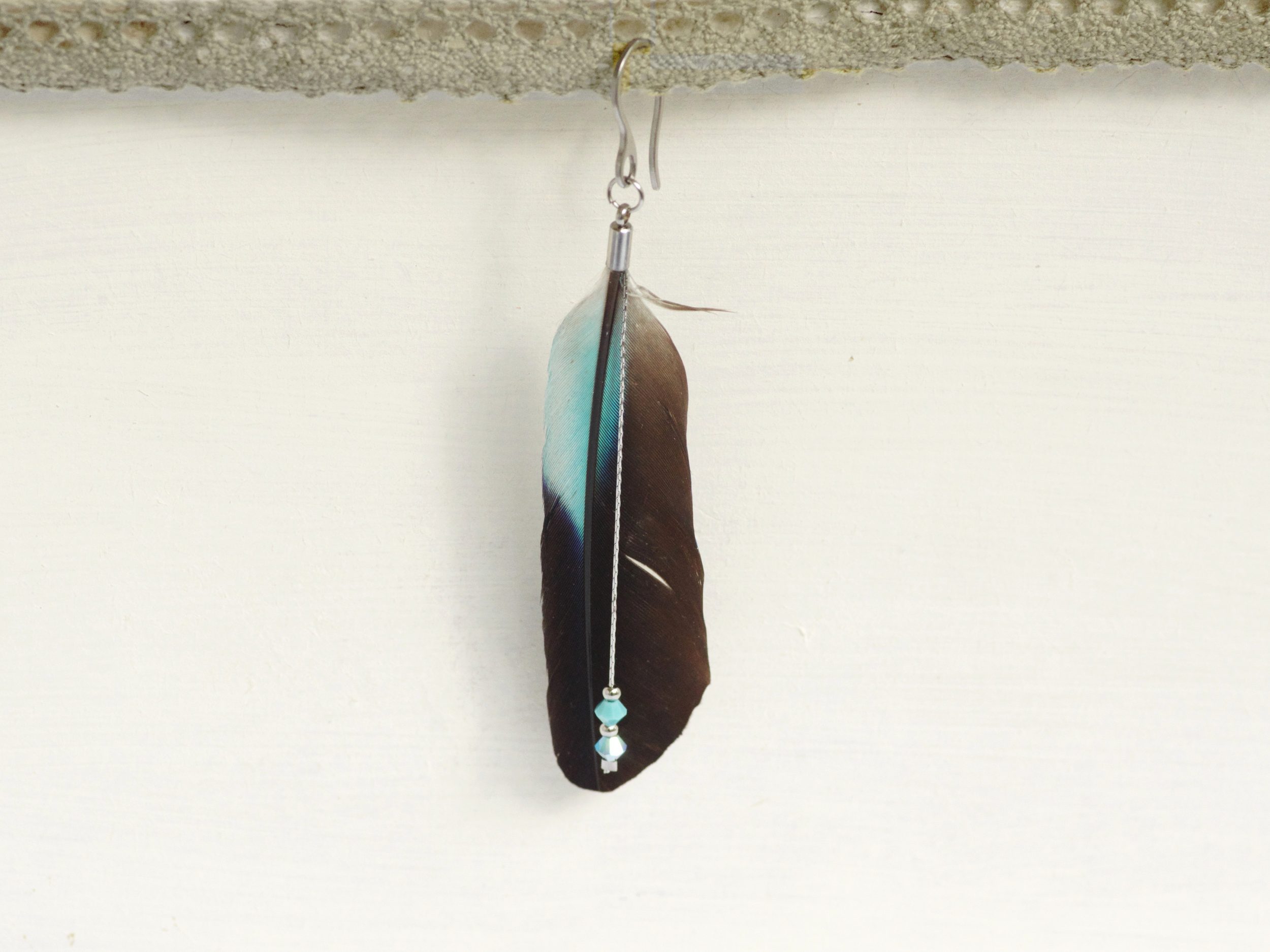 Boucle d'oreille réalisée avec une grande plume noire et bleue et des perles assorties