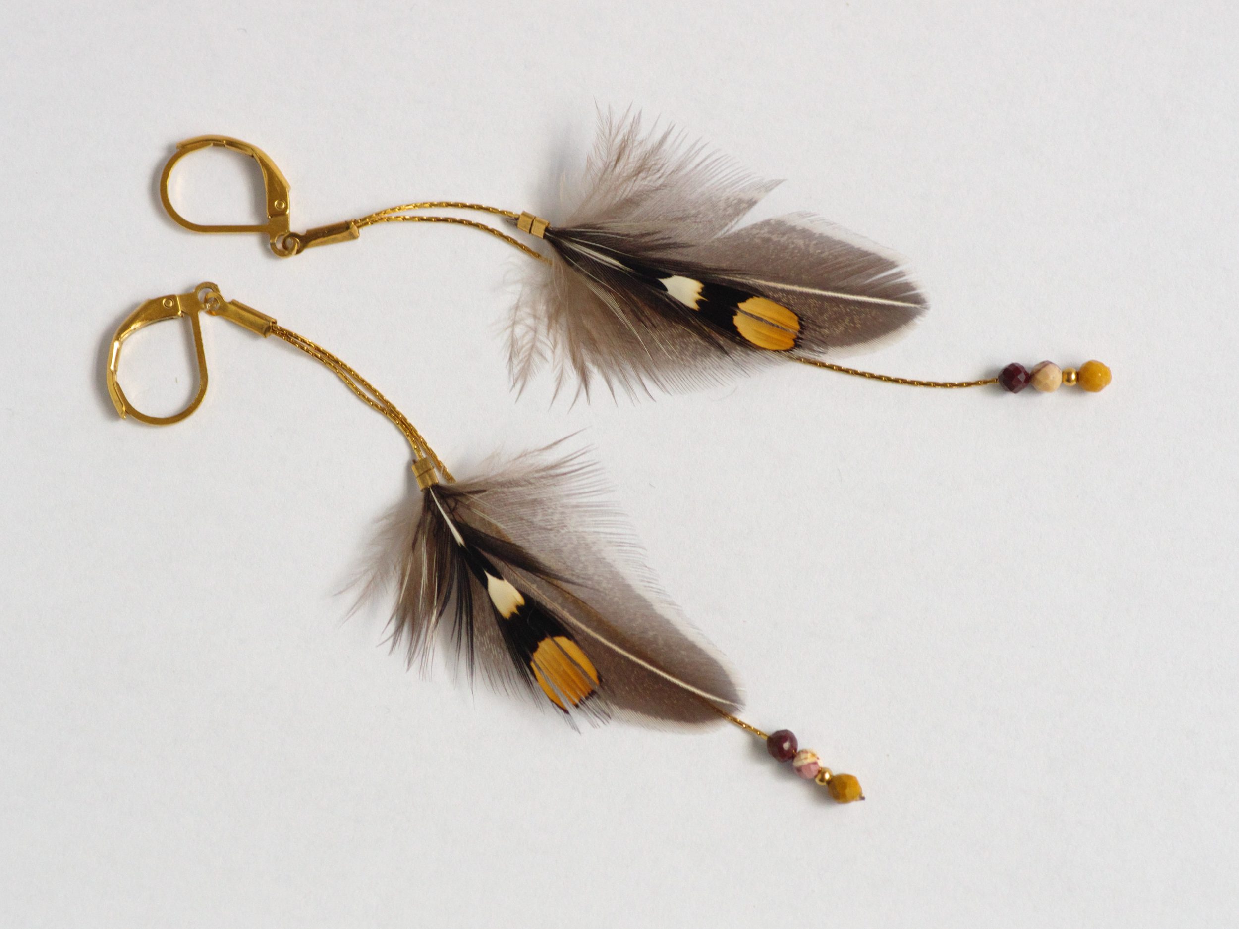 Boucles d'oreilles avec des plumes graphiques de jungle coq sur des fines chaînes dorées. Couleurs : gris noir blanc et ocre (coq de sonnerat).