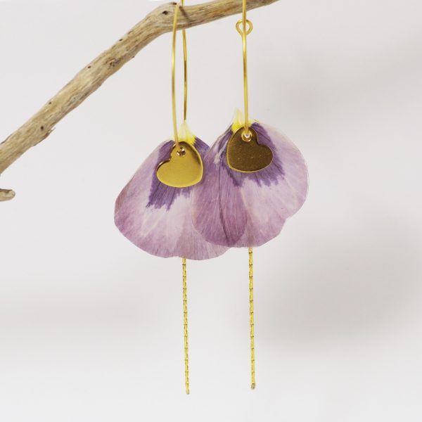 Des petits pétales violets sont enfilés sur des fines créoles dorées avec des petits cœurs et des chaines dorées.