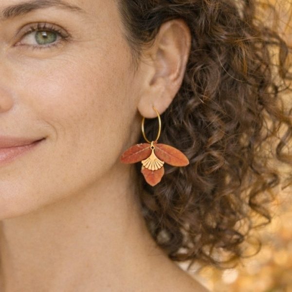 boucles d'oreilles avec petites feuilles rouges sur un anneau doré, portées par une femme naturelles. Image IA