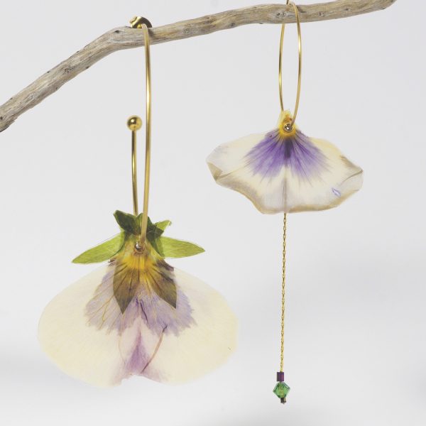 Deux pétales de pensées asymétriques montés sur des créoles dorées de tailles différentes. La composition est équilibrée par une chaîne et quelques perles.