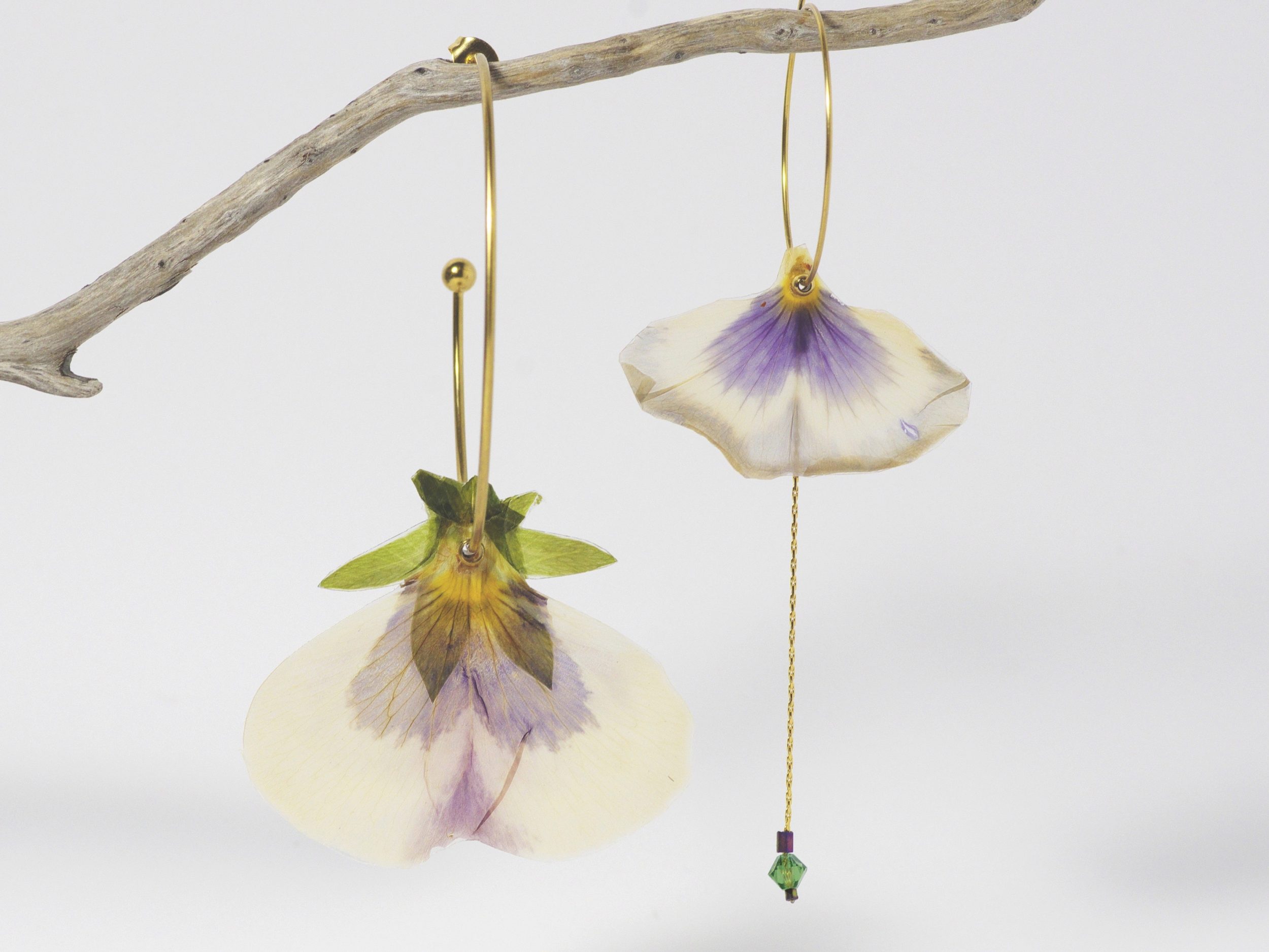 Deux pétales de pensées asymétriques montés sur des créoles dorées de tailles différentes. La composition est équilibrée par une chaîne et quelques perles.