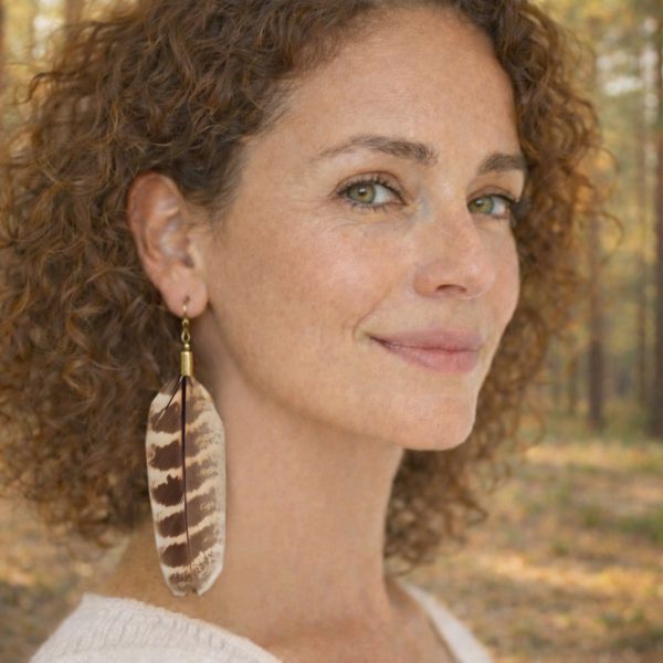 Boucle d'oreille avec une grande plume naturelle, portée par une femme dans une pinède. (création IA)