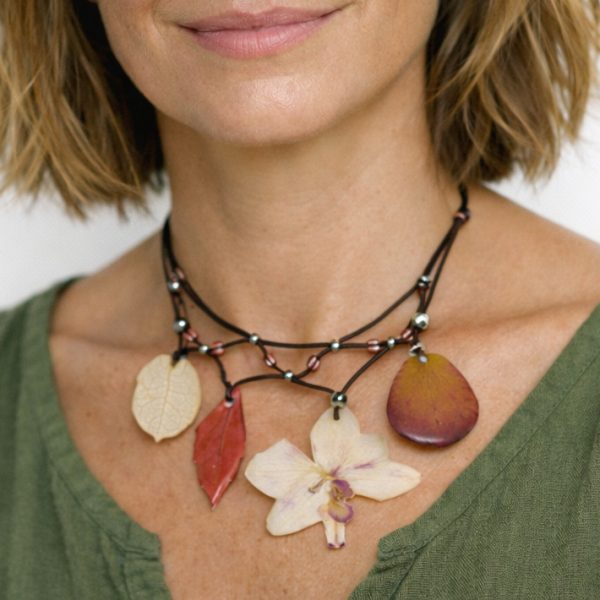 Collier fleuri de style bohème avec une orchidée et des pétales et feuilles dans des tons rouge blanc et rose pâle. (modèle IA)