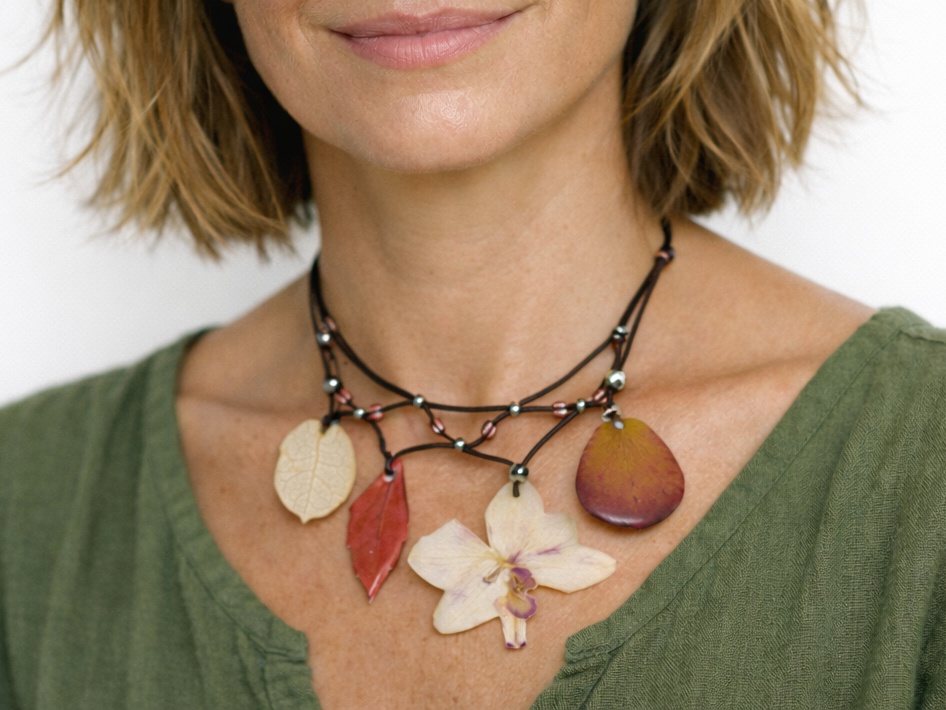 Collier fleuri de style bohème avec une orchidée et des pétales et feuilles dans des tons rouge blanc et rose pâle. (modèle IA)