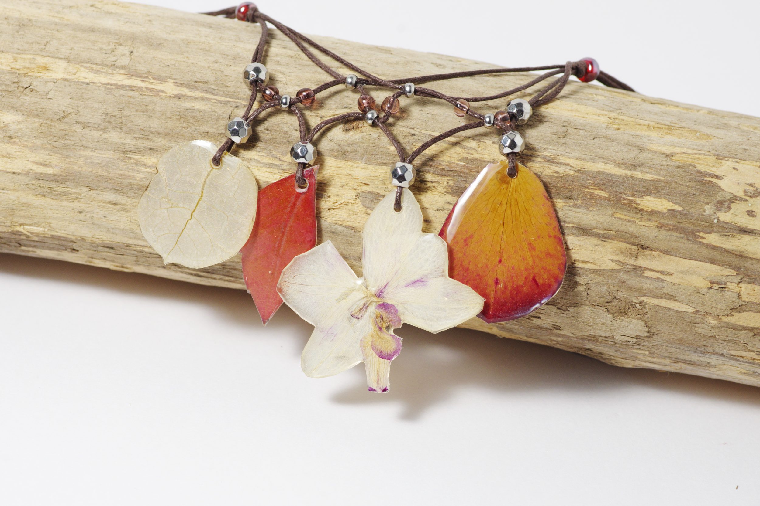 Collier fleuri de style bohème avec une orchidée et des pétales et feuilles dans des tons rouge blanc et rose pâle.