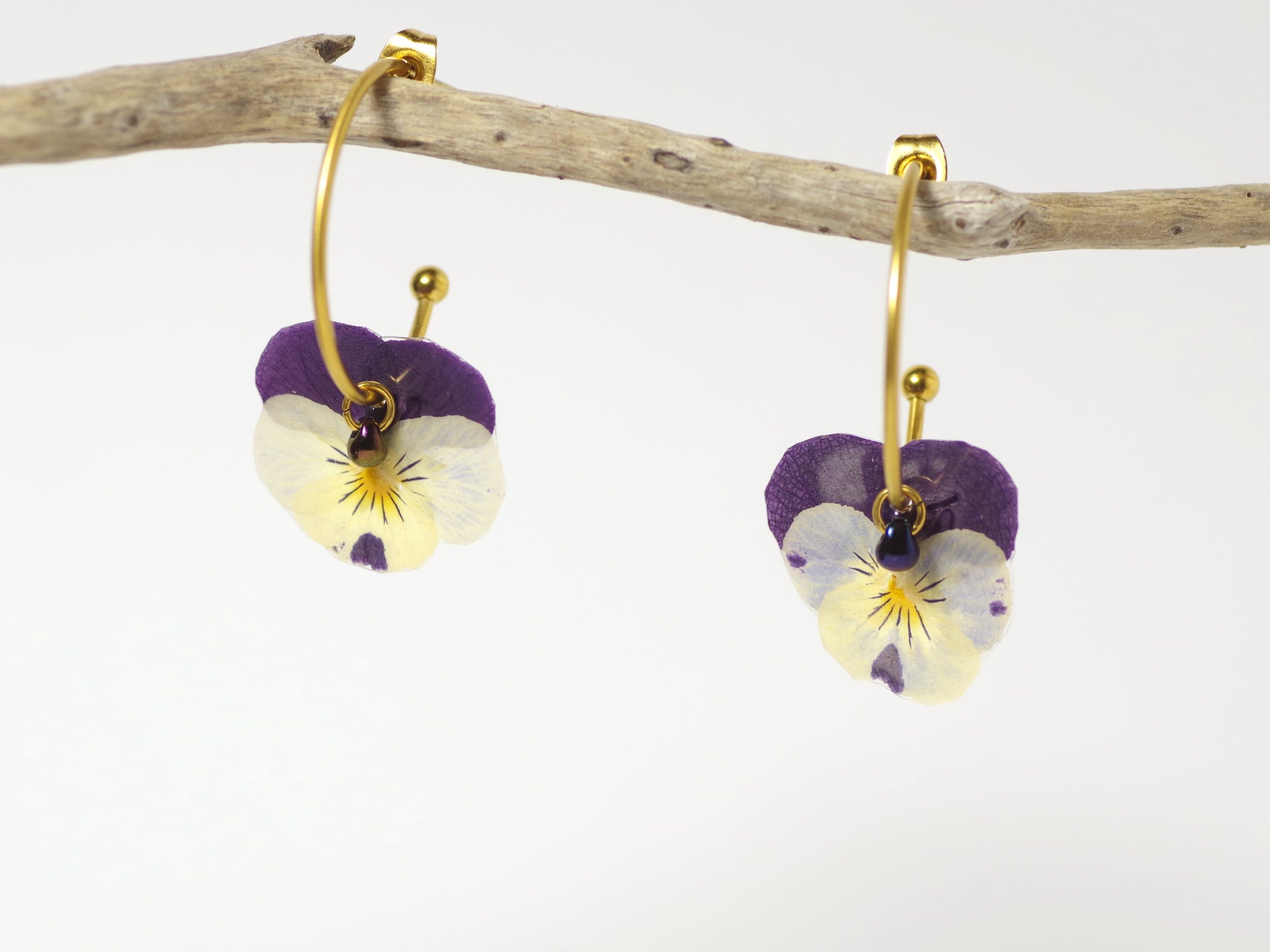 Minuscules pensées violettes et blanches sur des mini créoles dorées.