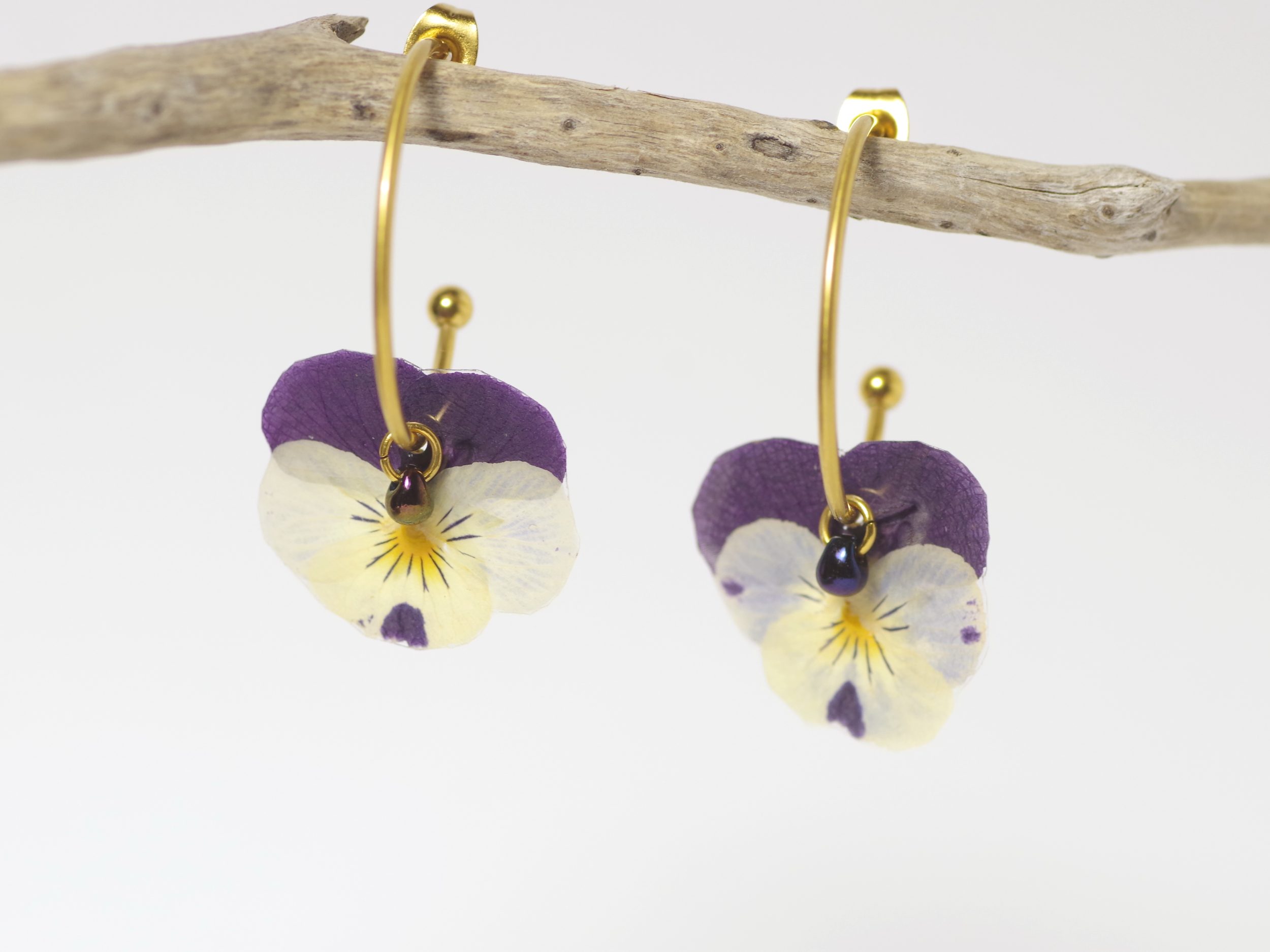 Minuscules pensées violettes et blanches sur des mini créoles dorées. Fleurs véritables.